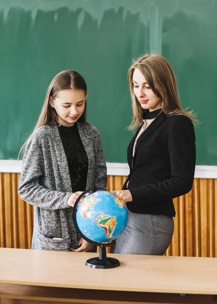 Una maestra y un estudiante observan juntos un globo terráqueo en el aula